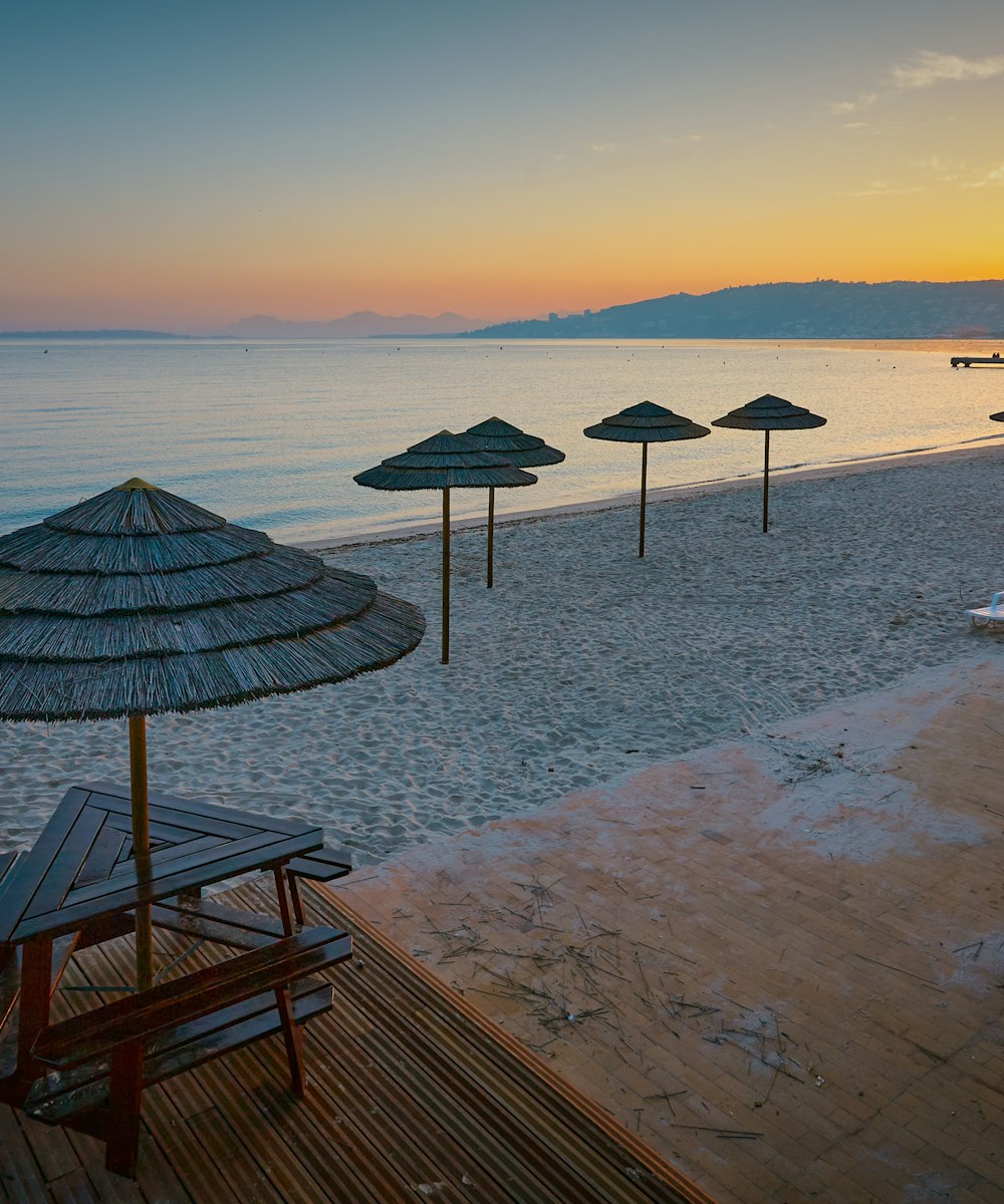 Plage de sable fin de Juan-les-Pins au coucher de soleil, parasols en bambou, Méditerranée et collines à l'horizon