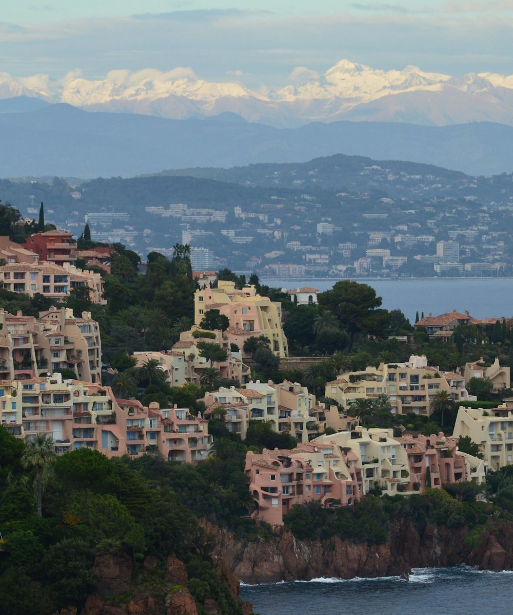 Résidences accrochées aux falaises rouges de l'Estérel à Théoule, Cannes en arrière-plan et Alpes enneigées à l'horizon